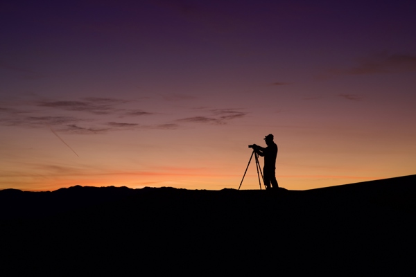 A photographer silhouetted at sunrise in the Mesquite Flats sand dunes of Death Valley, taken during a Muench workshop